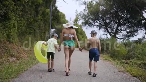 后景母亲和她的两个儿子在夏天阳光明媚的日子里在海滩附近的公园里散步一个穿泳衣的年轻女人和一个视频的预览图