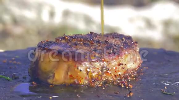 火煮多汁牛排香料中的一块肥肉倒入橄榄油在篝火上用热石炸视频的预览图