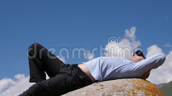 睡在石头上的疲倦的人背景是蓝色多云的天空视频的预览图