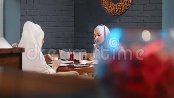 一位穆斯林妇女坐在餐桌旁的咖啡馆里一边吃东西一边聊天视频的预览图