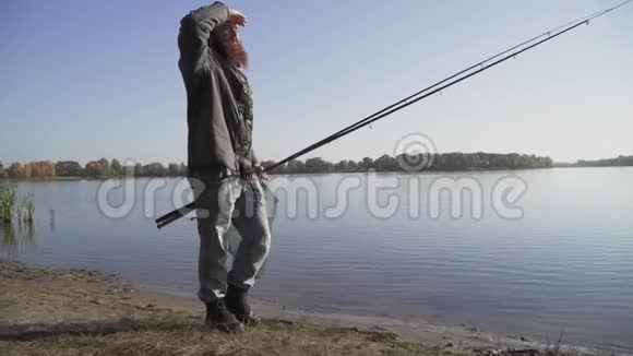 长胡子的成年渔夫带着钓竿和埋伏圈网在河边散步慢动作视频的预览图
