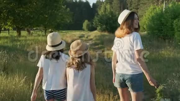 孩子们三个戴着帽子的女孩手牵着手沿着乡间小路走回来视频的预览图