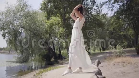 肖像可爱的年轻女孩一头长长的黑发穿着一件白色的夏季时装长裙站在海滨视频的预览图