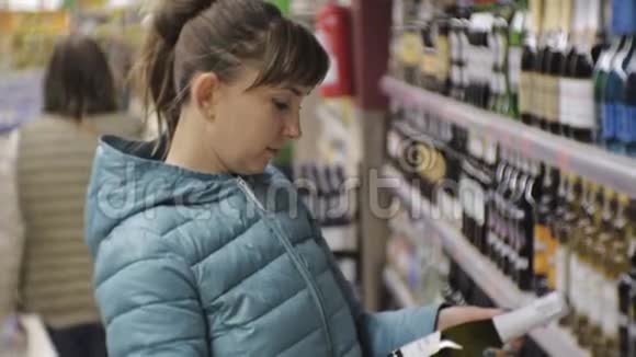 超市里的女人穿着蓝色夹克的年轻白种女人读着小瓶子上的标签选择起泡酒视频的预览图