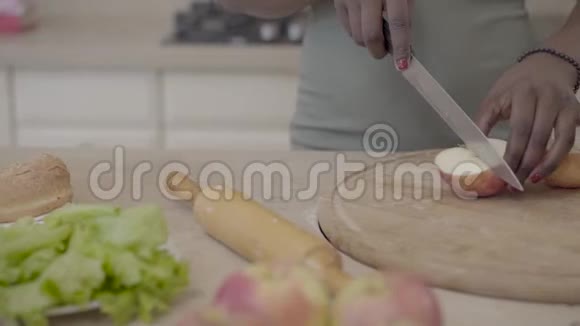 美国黑人妇女在现代厨房的背景上用刀在木板上切苹果关门视频的预览图