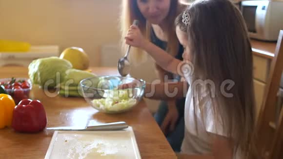 学龄前儿童在母亲的指导下在厨房里做沙拉女孩给蔬菜加盐加香料视频的预览图