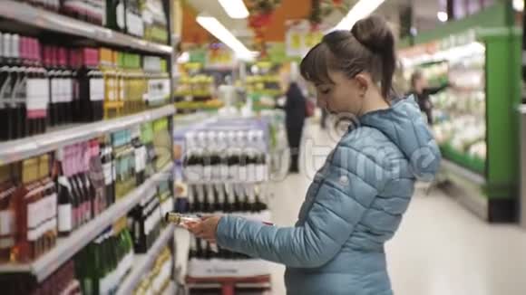 超市里的女人年轻的白种人穿着蓝色夹克在透明瓶子上看着标签选择白色视频的预览图