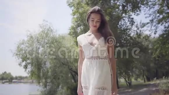 肖像可爱的年轻女孩一头长长的黑发穿着一件白色的夏季时装长裙站在海滨视频的预览图