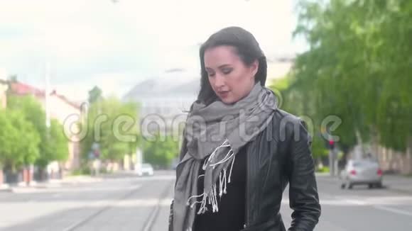 穿着黑色皮夹克的年轻女孩站在一条城市街道的背景上视频的预览图