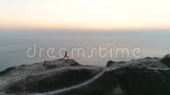 女人正在山顶上做瑜伽日落时可以看到海景空中镜头侧视视频的预览图