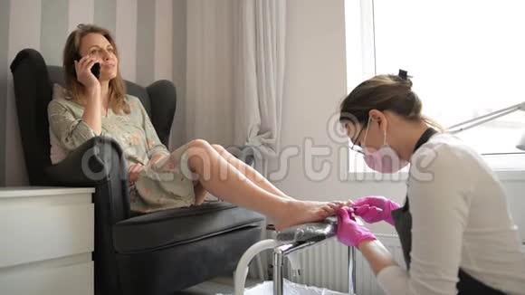 美丽的女人在水疗美容院得到专业的修脚师父正在清理她的指甲客户正在聊天视频的预览图