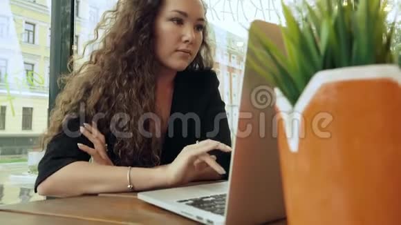 年轻的混血女人在咖啡馆里用笔记本电脑工作视频的预览图