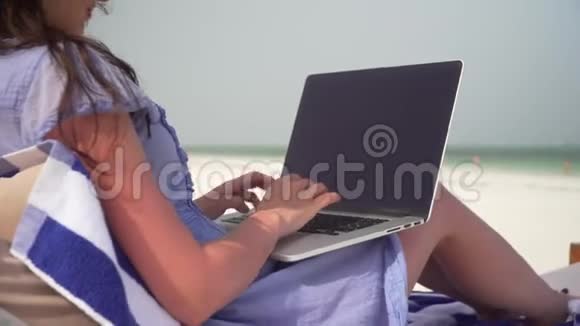 年轻女子在海边的白色沙滩上使用笔记本电脑视频的预览图