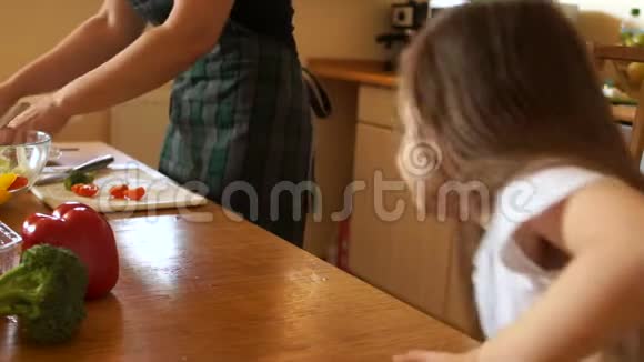 母亲在厨房里给女儿喂一顿健康的午餐孩子正在嚼樱桃西红柿妈妈很乐意视频的预览图