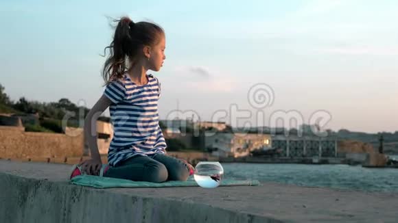 坐在岸边的小女孩宠物鱼圆形水族馆在户外夏天气候概念视频的预览图