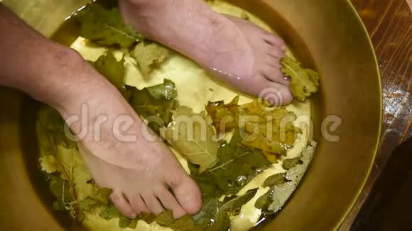 男人脚在带有橡木叶子的修脚浴中视频的预览图
