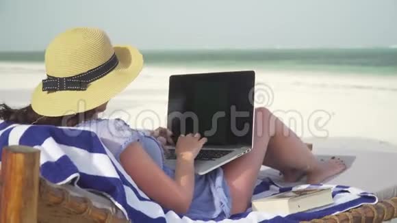 年轻女子在海边的白色沙滩上使用笔记本电脑视频的预览图