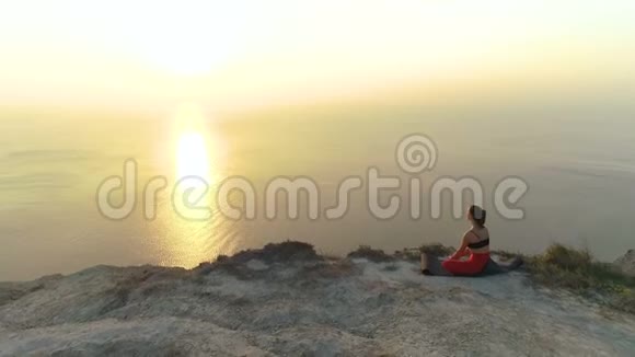 美丽的风景女人做瑜伽巴达科纳萨纳捆绑角度波塞在山上与海景在日落视频的预览图