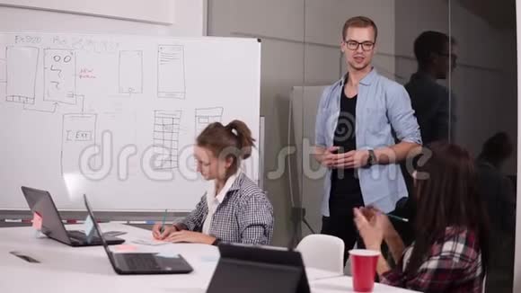 在商务会议期间穿格子衬衫的年轻女性与会议室的同事分享她的观点专业人员小组视频的预览图