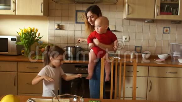 一位年轻的家庭主妇抱着一个婴儿喂养一个学龄前的女儿妈妈有两个孩子母亲节视频的预览图