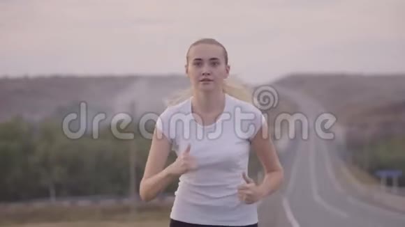 健康的生活方式日落时分一个穿着白色t恤的女孩在从城市出发的路上奔跑头发随风飘扬视频的预览图