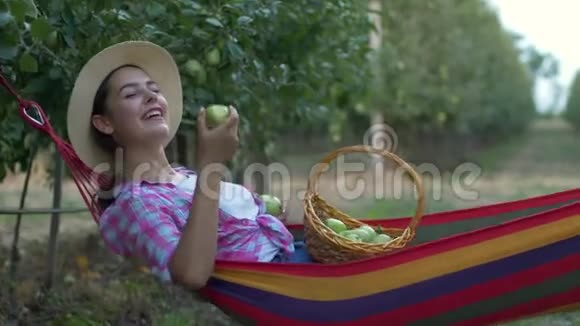 在花园里休息快乐的女孩躺在吊床上在收获的过程中吃苹果视频的预览图