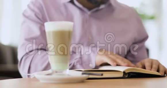 一个人正在看一本书他的手指在书页上坐在咖啡馆里前面是一杯卡布奇诺视频的预览图