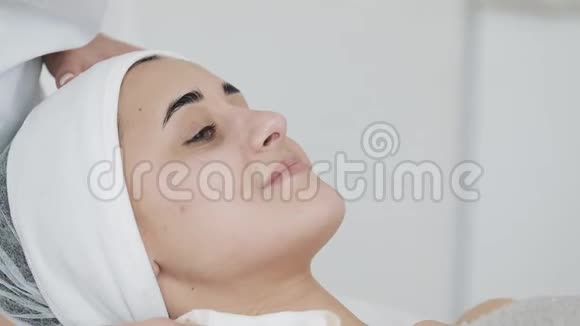 美丽的女人在水疗沙龙按摩她的脸之前用餐巾擦拭她的脸慢动作视频的预览图