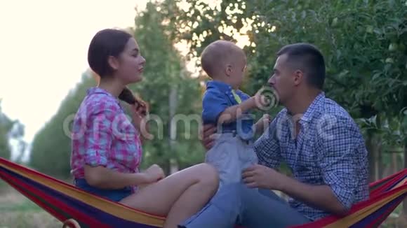 幸福的农村家庭肖像微笑的爸爸妈妈和小儿子在吊床上放松时放弃拇指视频的预览图