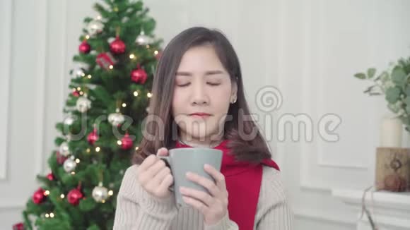 快乐的年轻亚洲女人在圣诞节的时候在家里的客厅里抱着温暖的咖啡微笑着对着镜头视频的预览图