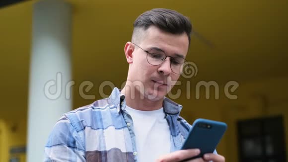一位英俊的年轻人用智能手机在社交媒体上滚动以设备笑声和视频的预览图