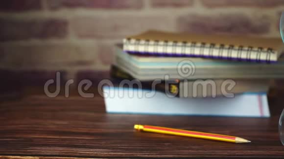 慢动作娃娃沙漏铅笔和书堆放在木桌上视频的预览图