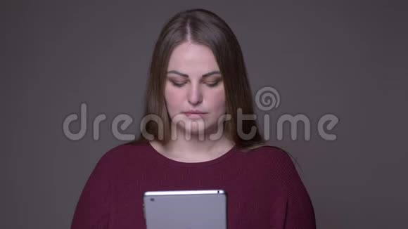 白种人年轻女性超重的特写镜头使用灰色背景的平板电脑视频的预览图
