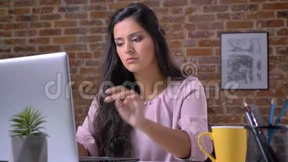 一个年轻忙碌的女孩正在阁楼办公室里用笔记本电脑工作打字喝咖啡从杯子里喝一口一块砖头视频的预览图