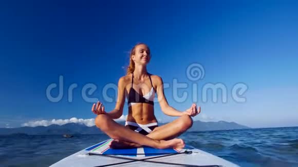 穿比基尼的女孩在海洋的桨板上做瑜伽姿势视频的预览图