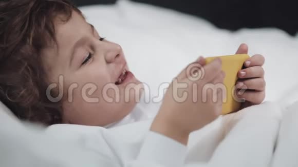 小男孩在哭后用药片摩擦她的眼睛他躺在床上手里拿着一部黄色的智能手机视频的预览图