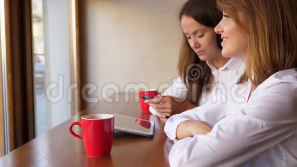 两个女人在咖啡馆聊天使用智能手机和平板电脑视频的预览图