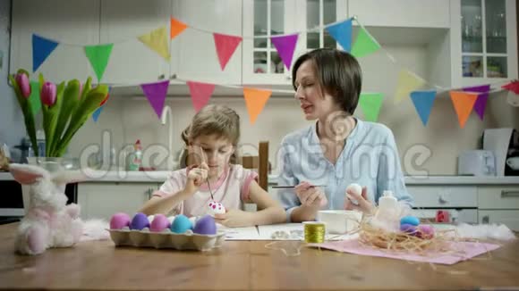 母女俩坐在餐桌旁一起用彩蛋做窝在厨房里嬉戏视频的预览图