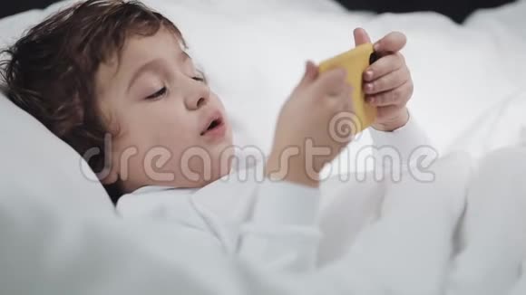 小男孩在哭后用药片摩擦她的眼睛他躺在床上手里拿着一部黄色的智能手机视频的预览图