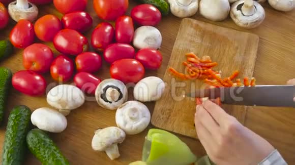 女人手在厨房桌子上的木板上用蔬菜切红胡椒视频的预览图