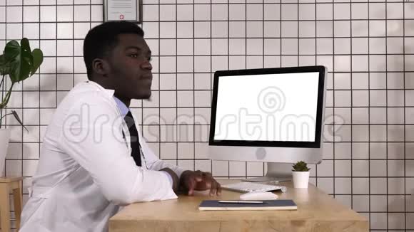 无聊的非洲医生在电脑屏幕旁等着什么白色显示器视频的预览图