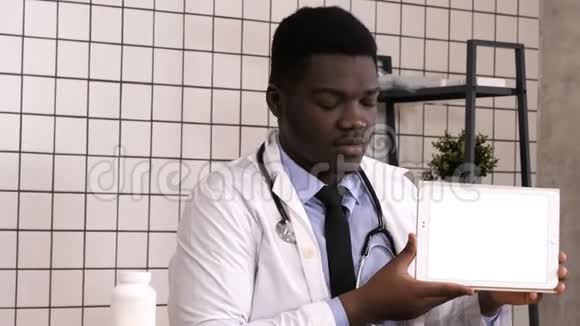 英俊严肃的非洲医生在平板电脑屏幕上展示产品白色显示器视频的预览图
