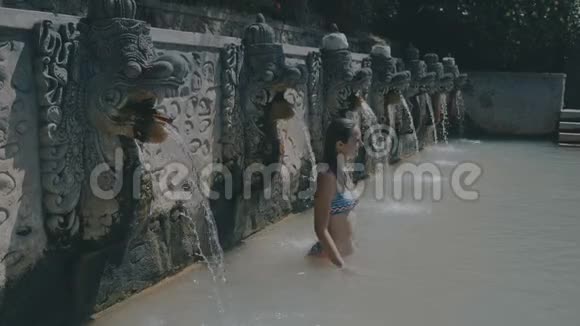 巴厘岛温泉里的一位在水流下的年轻女子视频的预览图