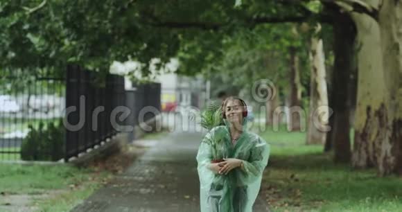 快乐的漂亮小伙子在雨天走在街上捧着一朵绿花听着耳机里的音乐视频的预览图