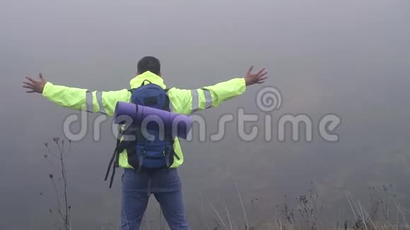 一位背着背包的游客站在山的边缘在雾中挥舞着双手慢悠悠地视频的预览图