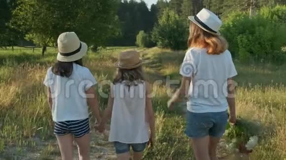 孩子们三个戴着帽子的女孩手牵着手沿着乡间小路走回来视频的预览图