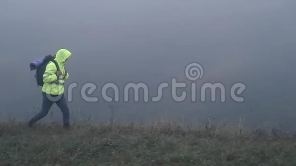 一个身穿信号背心头罩背着背包的游客在雾中慢悠悠视频的预览图