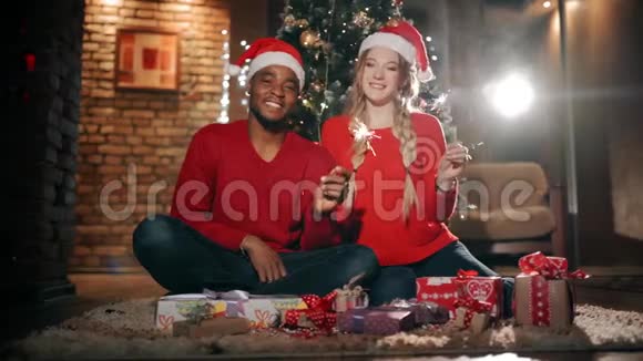 新年礼物中一个幸福的家庭正坐在圣诞树附近一对微笑的夫妇在挥舞着火花视频的预览图