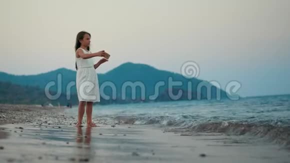 日落时分在海边的智能手机摄像头上摆姿势的小女孩视频的预览图