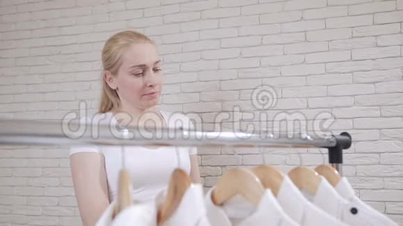 靠近衣架的女人选择并试着穿白色衬衫照镜子视频的预览图
